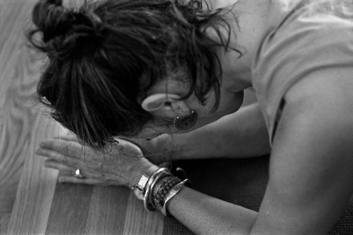 A person bowed forward, forehead resting on hands and hands on a wooden bench.