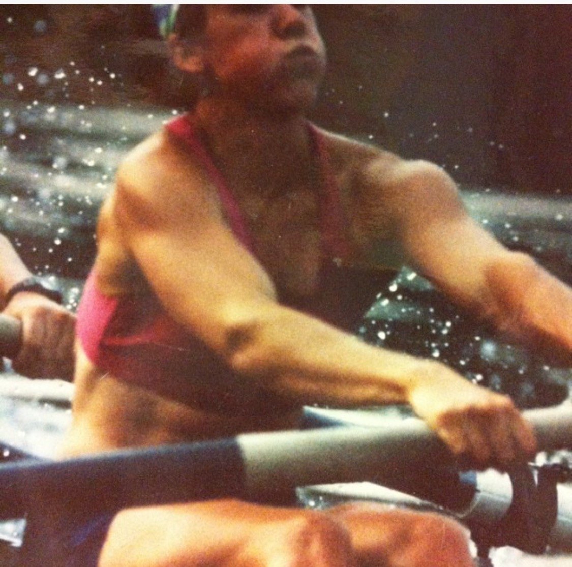 Katie Cooley rowing, mid-stroke, water spraying from the oar.